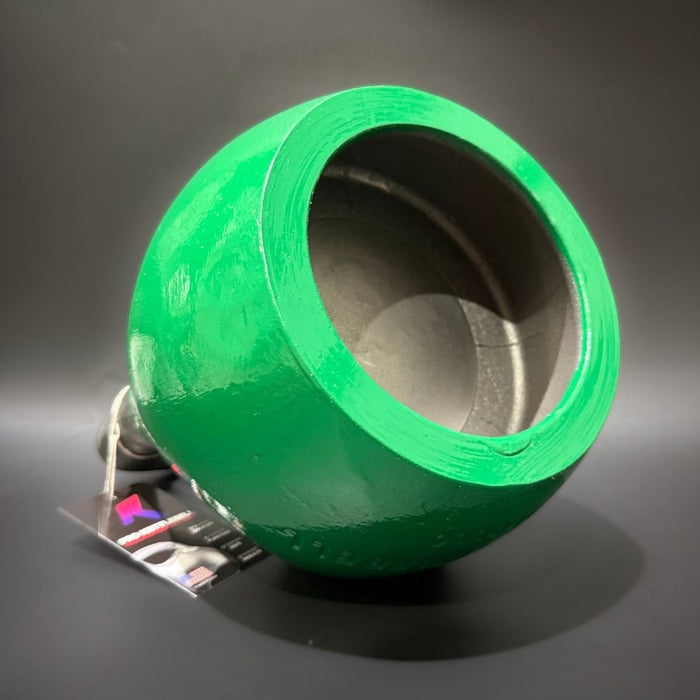 A bright green kettlebell with a wide open tbottom, photographed on a dark gray studio background. A small attached tag is visible near the base.